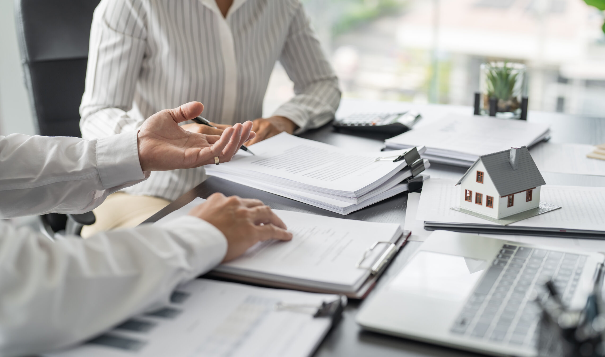 Zwei Personen besprechen kommunales Immobilienmanagement mit Unterlagen und Hausmodell auf dem Tisch.