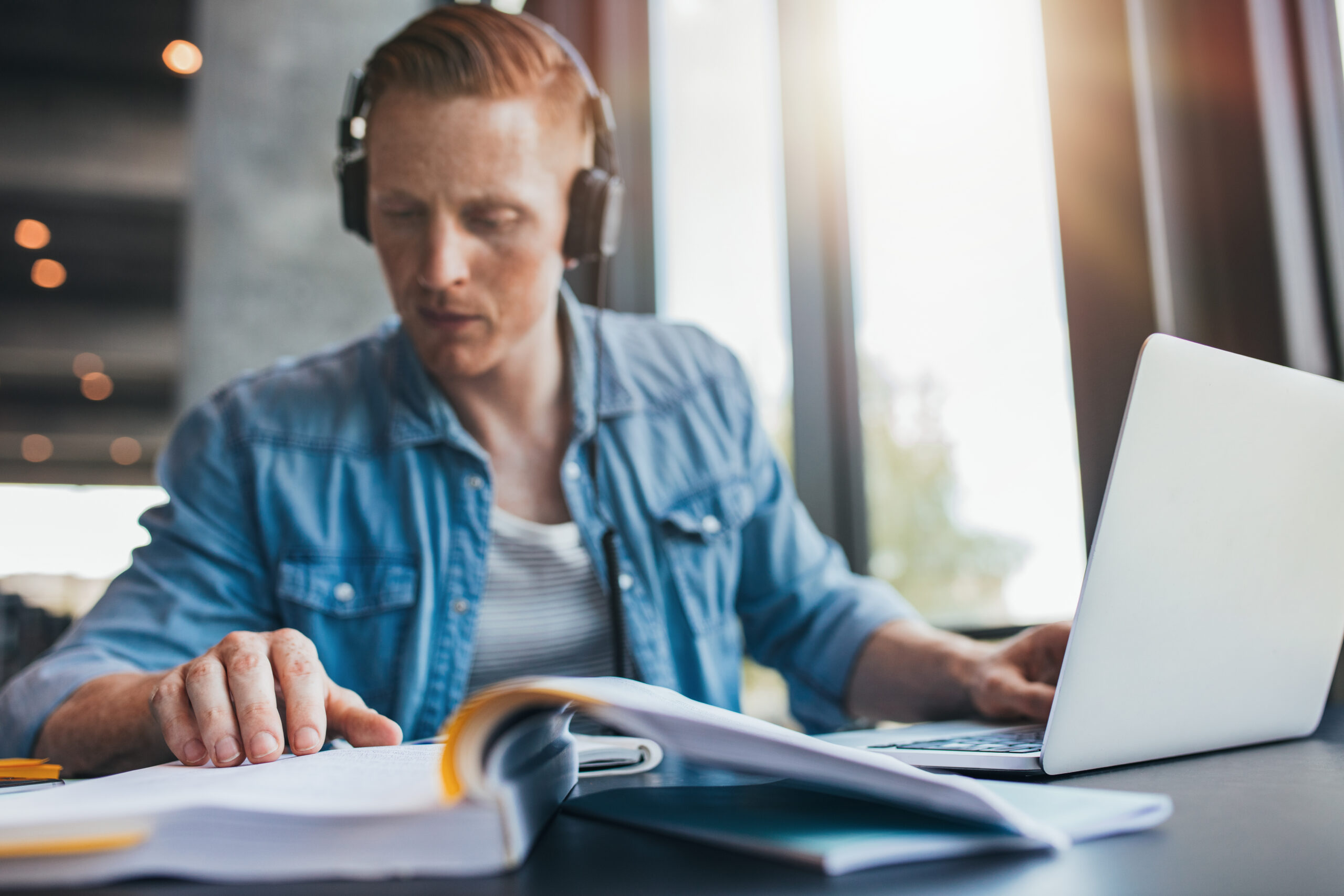 Lehrgangsteilnehmer lernt konzentriert mit Laptop, Kopfhörern und aufgeschlagenem Buch.