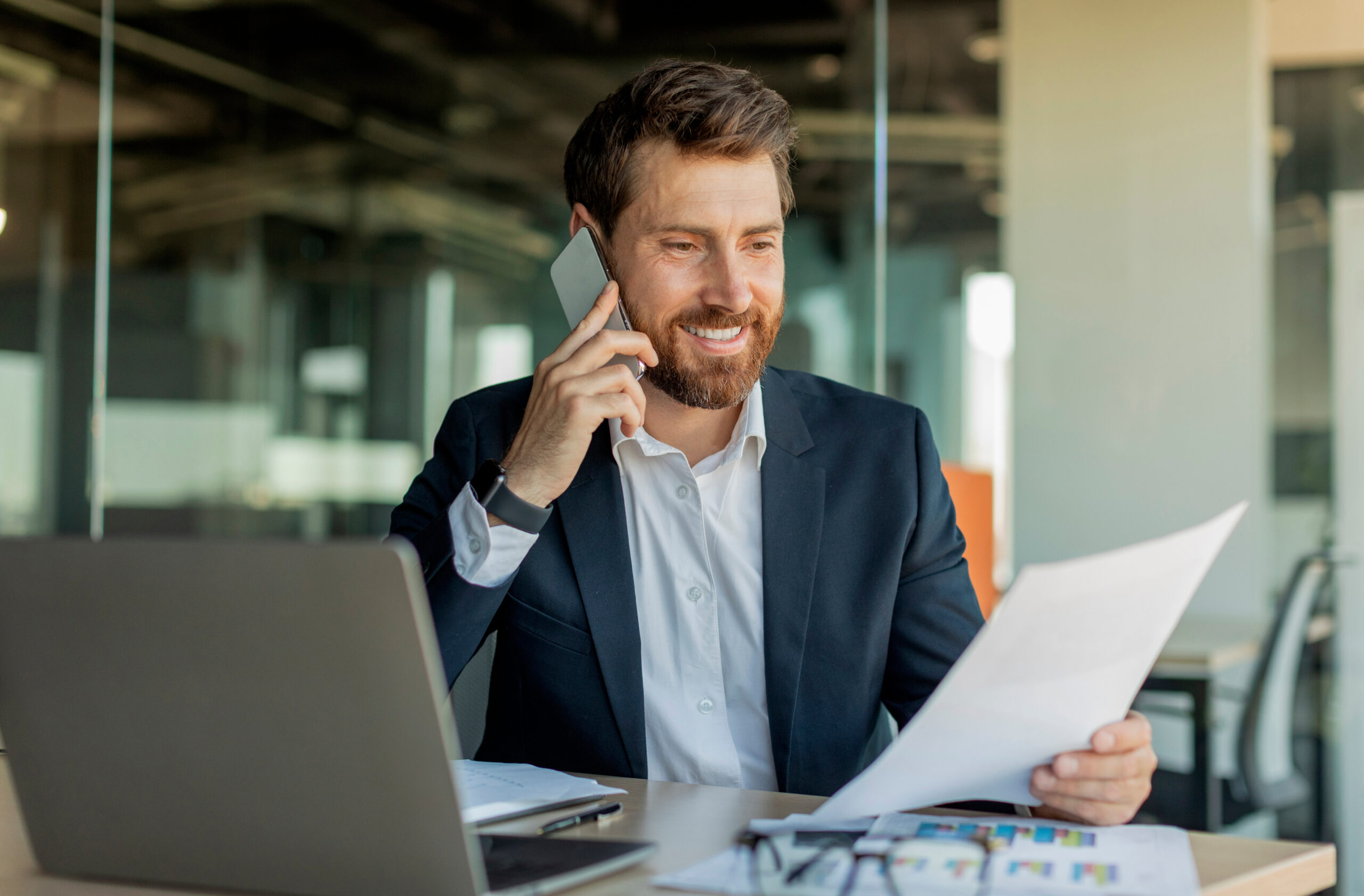 Kommunale Fachkraft für Finanzen telefoniert im Büro und prüft Finanzdokumente mit Laptop und Diagrammen.