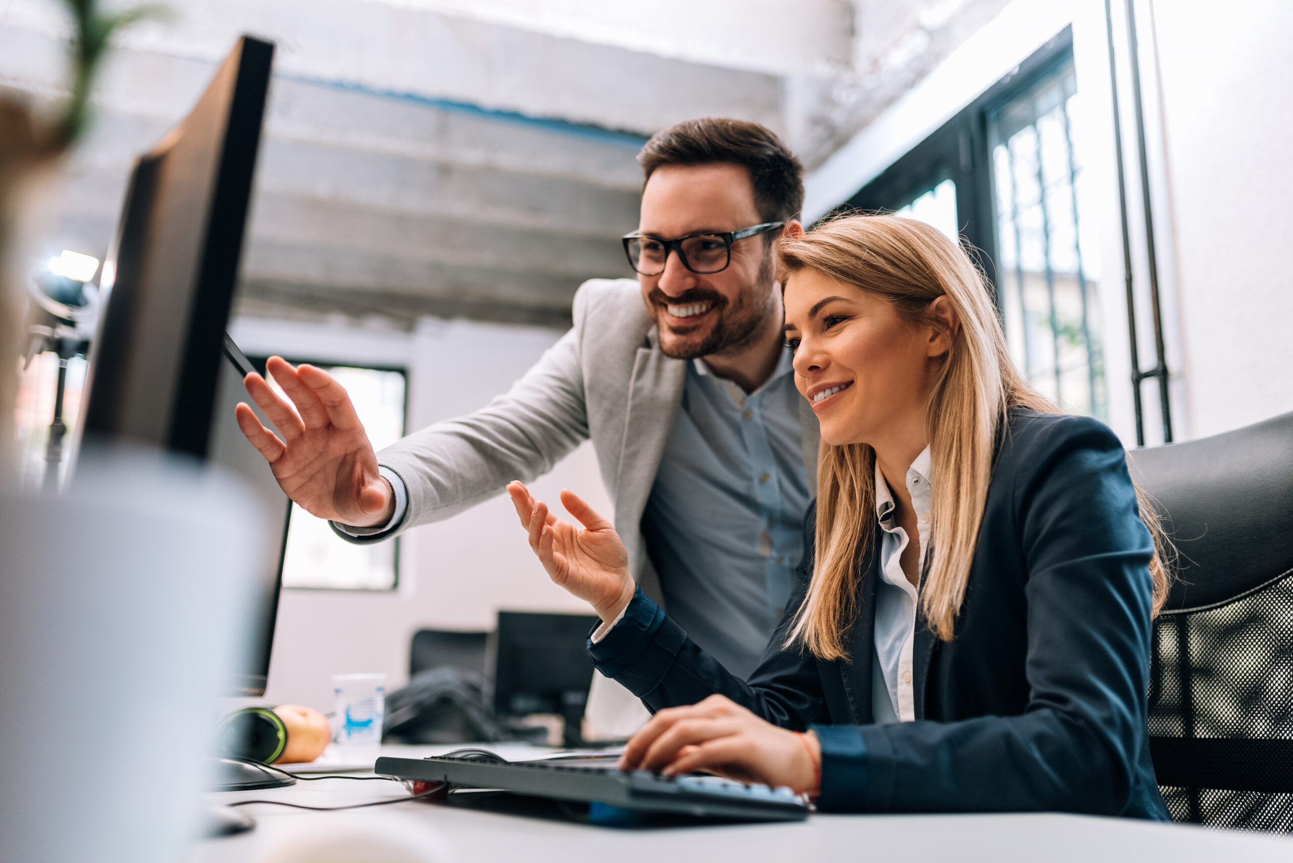 Mann und Frau im Büro arbeiten gemeinsam am Computer und lächeln.