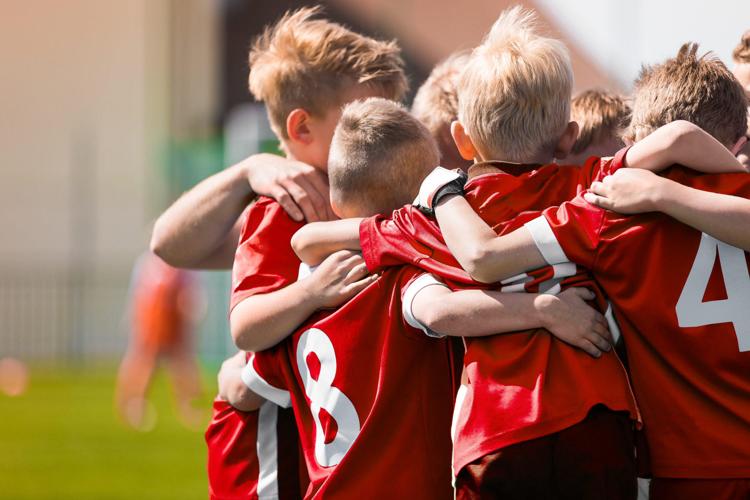 Fußball-Kinderteam in roten Trikots bildet einen Kreis und zeigt Zusammenhalt.