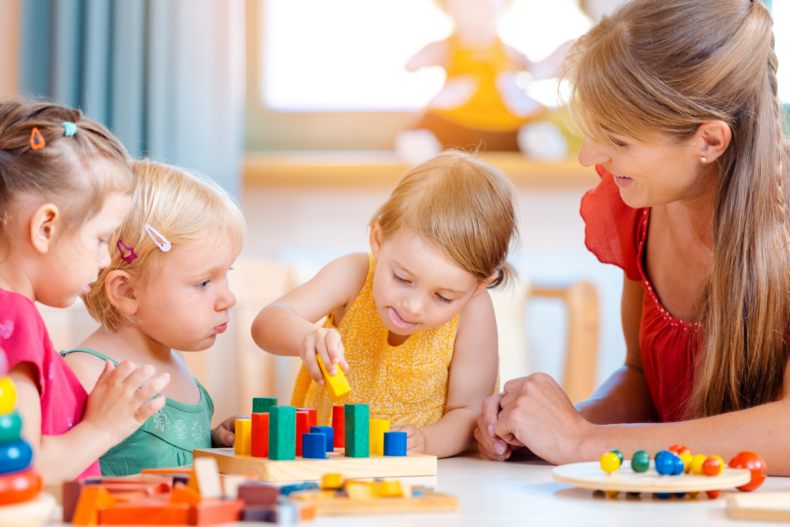 Kinder spielen im Kindergarten mit bunten Holzbausteinen und werden von Erzieherin begleitet.