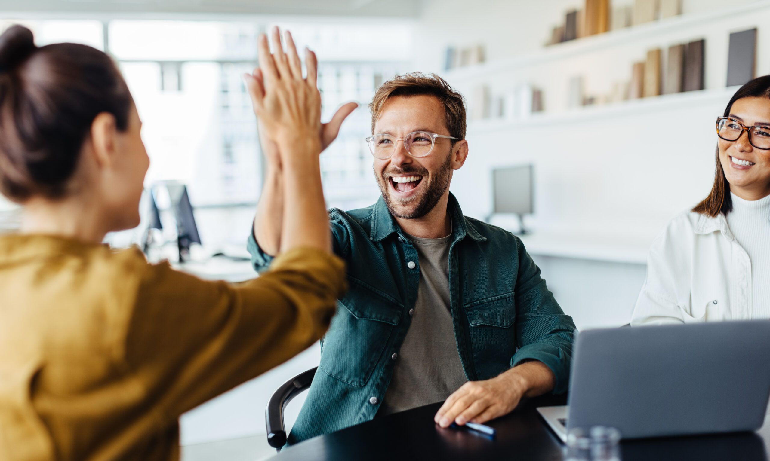 Lachende Verwaltungskollegen geben sich im Büro ein High Five zur Feier erfolgreicher Teamarbeit