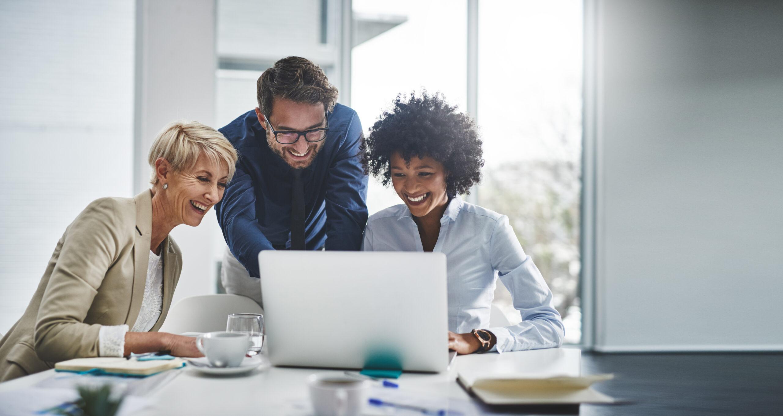 Mehrere Personen arbeiten gemeinsam an einem Laptop in einem Büro und stimmen sich zu Inhalten und nächsten Schritten ab.
