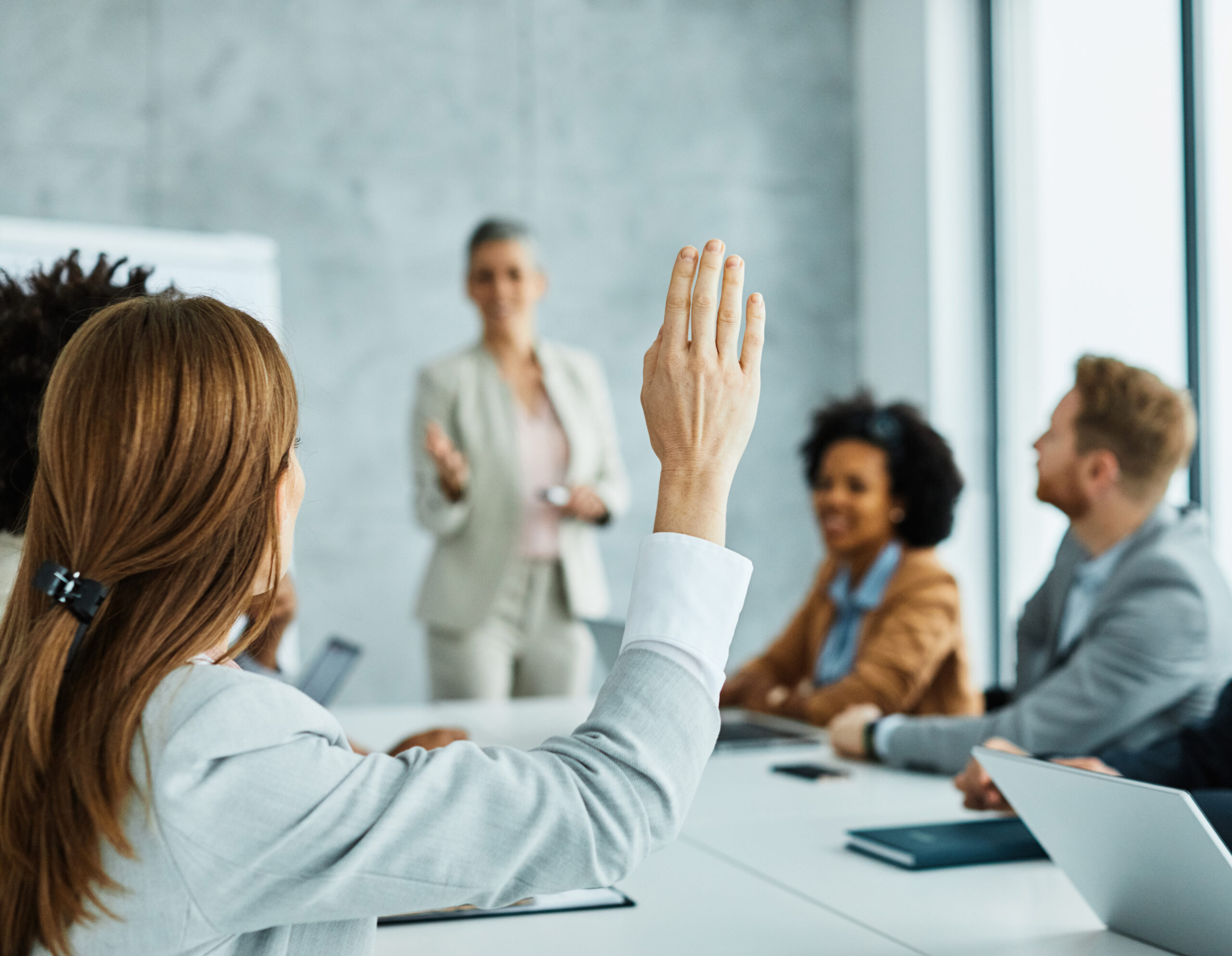 Neueinsteigerin der kommunal Verwaltung hebt Hand im Meeting.