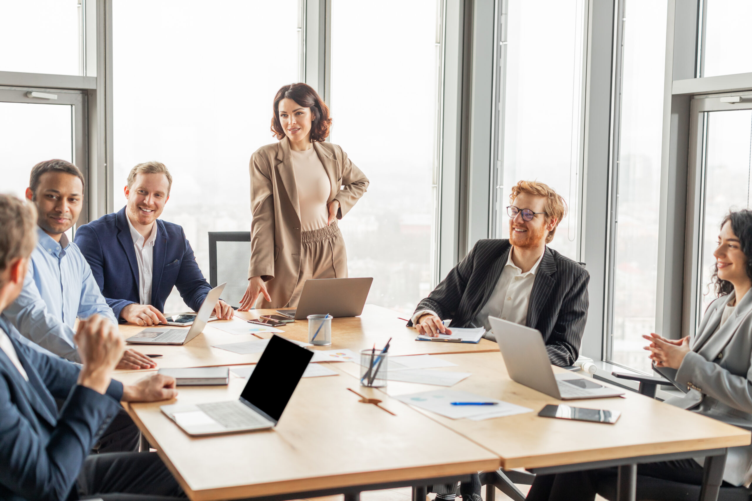 Gremienteam im Konferenzraum, Frau führt Meeting mit Gremienkollegen an großen Fenstern im modernen Büro.